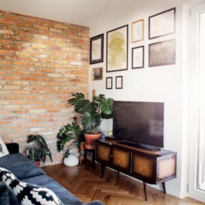 stylish-scandinavian-open-space-with-living-room-with-design-sofa-and-tv-table-bright-and-sunny-room-with-red-brick-wall-posters-composition-and-brown-wooden-parquet