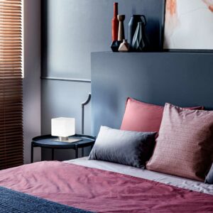 close-up-of-a-double-bed-decorated-with-pillows-in-a-hotel-room-interior-with-grey-wall-lamp-vases-and-window-blinds