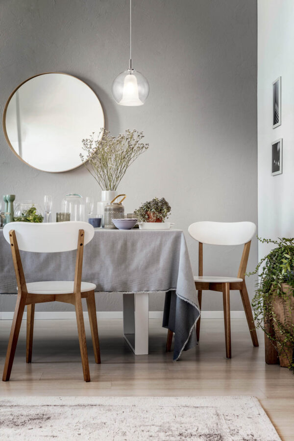 lamp-above-white-chairs-and-table-in-grey-dining-room-interior-with-plants-and-round-mirror-real-photo